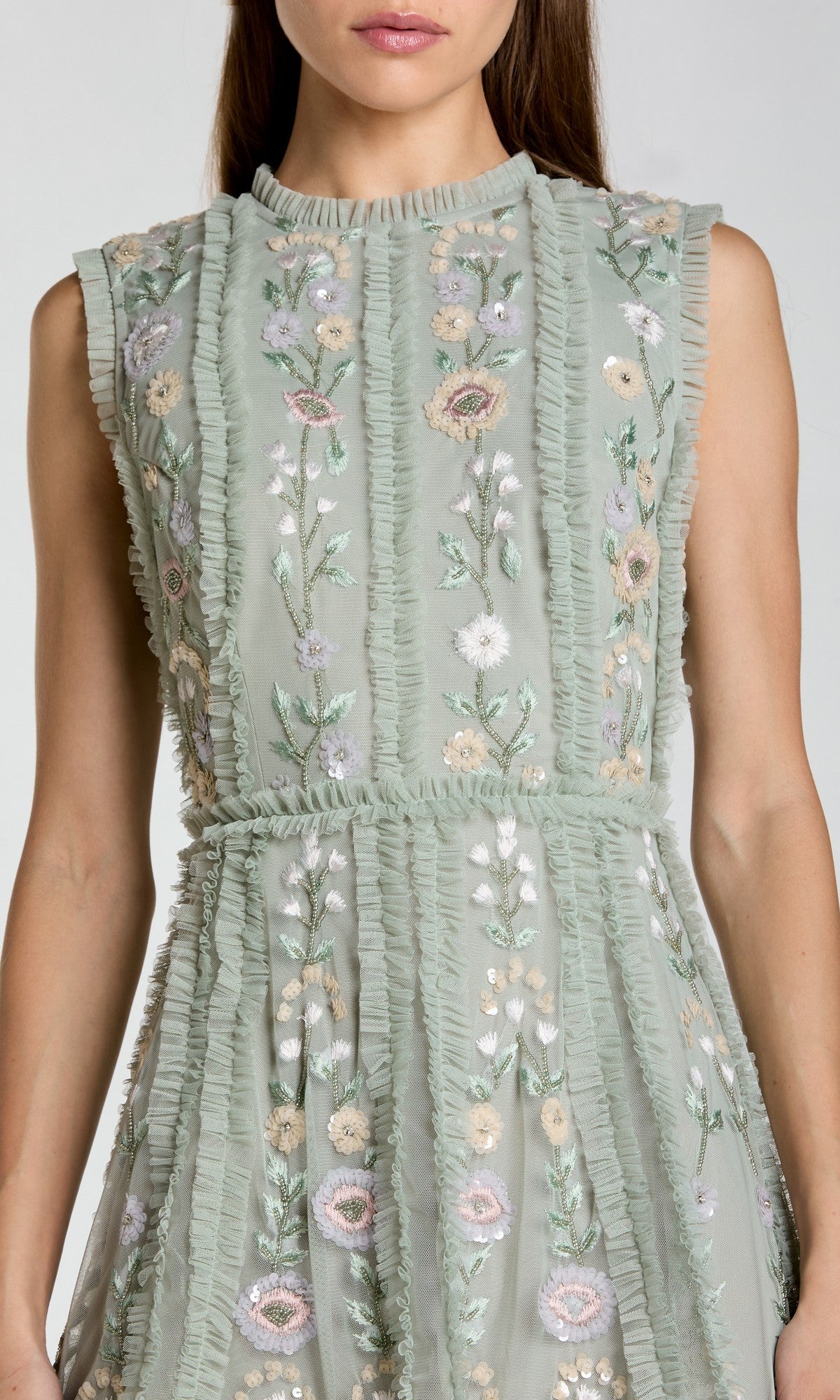 A woman wearing the Mac Duggal 9135, an embroidered short party dress with a sleeveless light green design and vertical ruffle details.